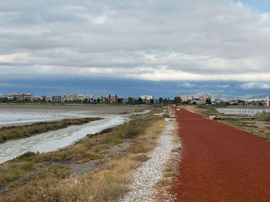 resiliente Landschaft mit Auenbereich, sandigem Ufer und roten Sandweg. Häuser im Hintergrund